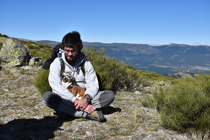 Hombre sentado en la naturaleza con su perro entre las piernas abrazados